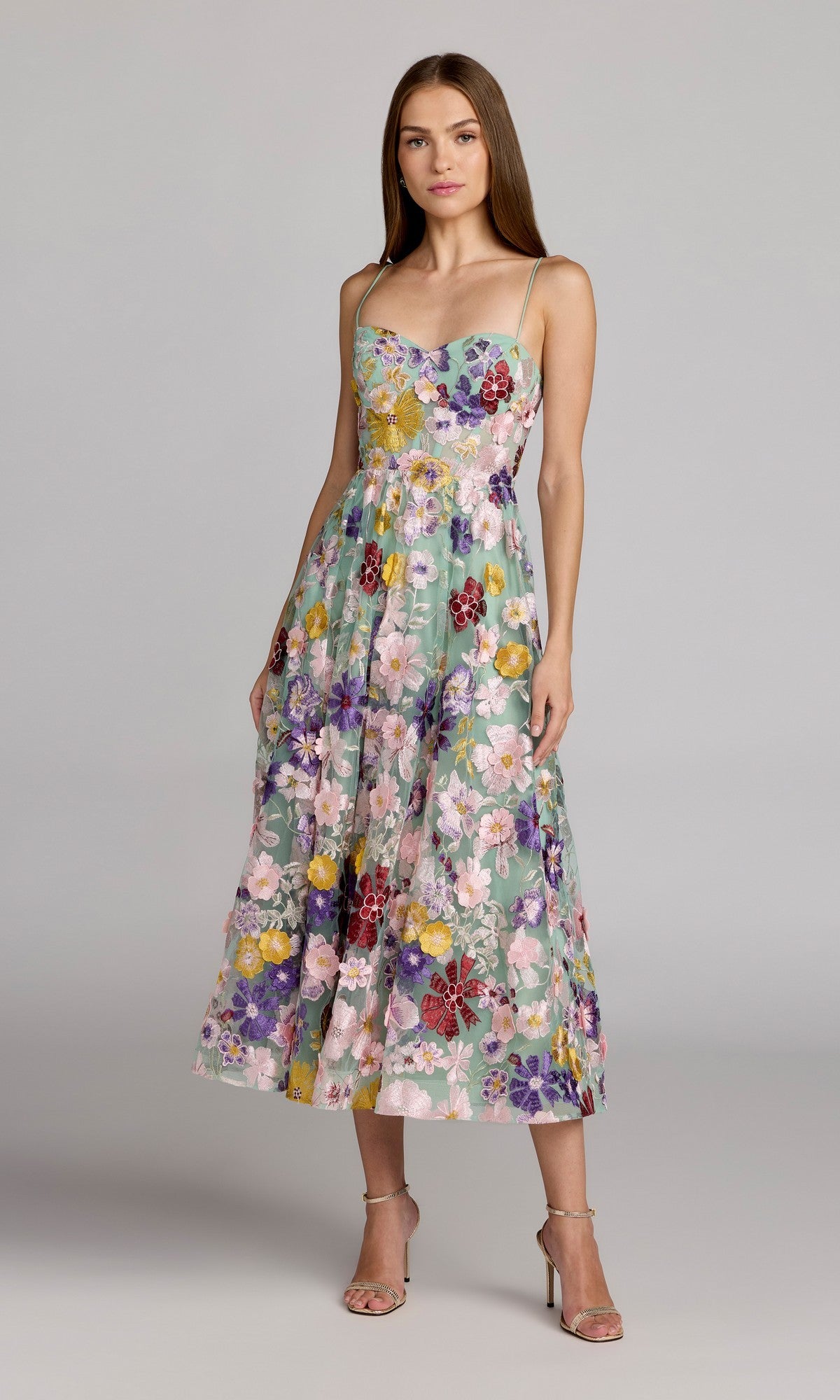 A woman stands wearing the Tea-Length Party Dress: Mac Duggal 68605 in Sage Multi. The dress features a structured bodice with thin straps, a colorful floral print, and an elegant A-line tea-length skirt, which she stylishly pairs with nude heels.